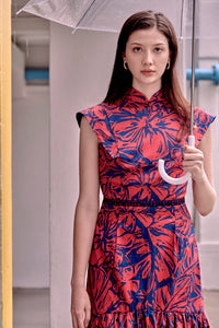 Eurasian lady holding an umbrella wearing a cheongsam dress in navy blue and red floral prints. Dress has large leaves and flowers print with a panel sleevs and A line tiered skirt. It also has a stand up mandarin collar and lace trimmed waist.