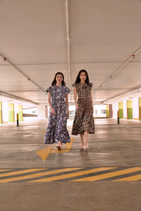 Two ladies walking in an empty carpark. Lady on left is an Eurasian, and wears a blue batik maxi dress, lady on right is of chinese descent, and wears a brown and white batik midi dress.