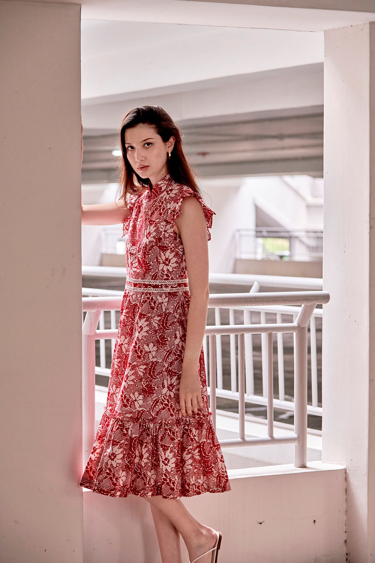 Side profile of Eurasian model, she is modelling a Dayglow red and white batik qipao dress. The dress is over her knee and has a frilly hem and laced trimmed waist band.